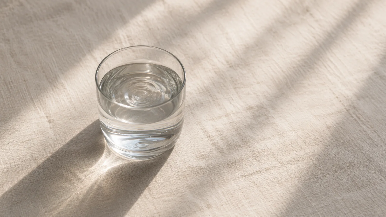 Vaso de agua sobre un mantel de lino, con sombras suaves de luz de ventana