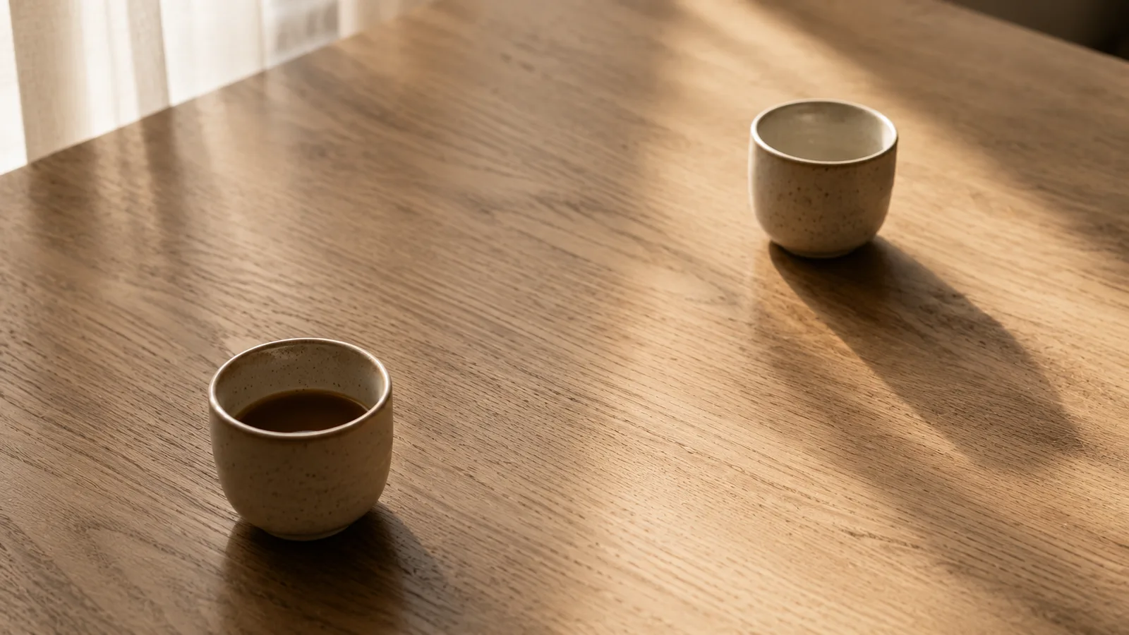 Dos tazas de cerámica sobre una mesa de madera, una cerca y otra distante